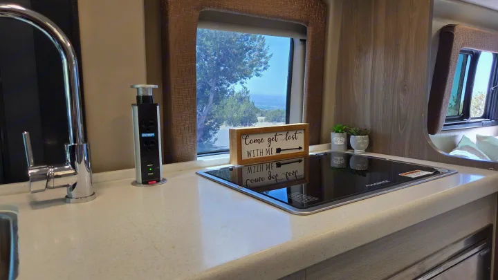 Enjoy an RV rental's modern kitchen, featuring a pop-up outlet, induction cooktop, and a scenic nature view from the window.. Thor Tellaro 2022