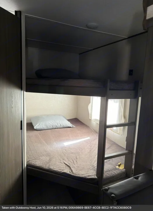 Interior of an RV rental featuring comfortable bunk beds with soft bedding and natural light from a window.. Forest River Shasta 2021