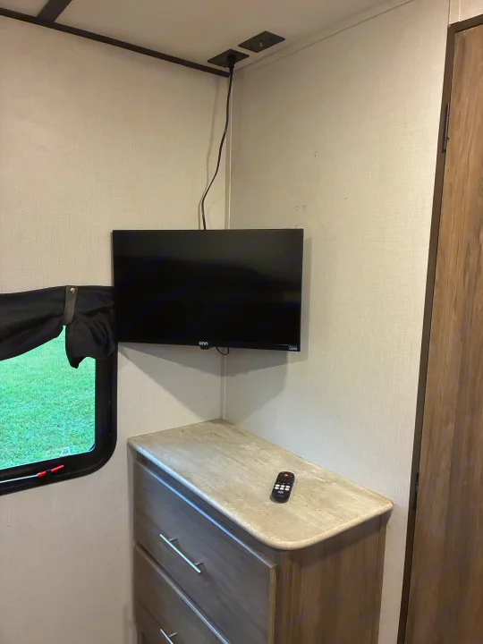 RV rental interior corner featuring a wall-mounted TV, dresser, remote, and window with a view of grass.. Crossroads RV Zinger 2021