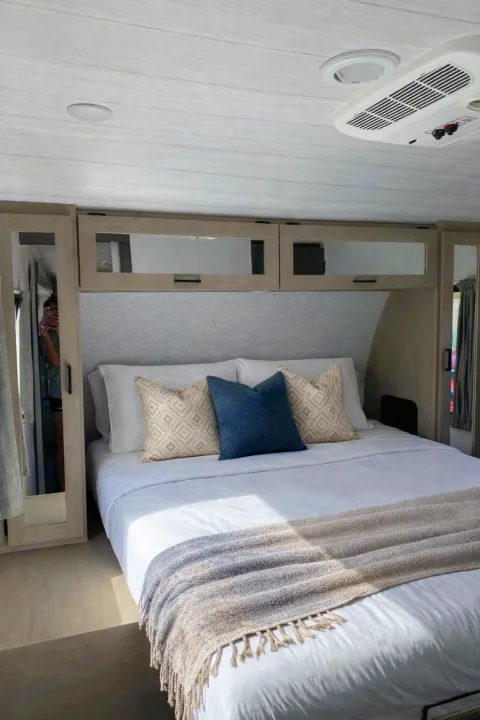 Experience comfort in this RV rental bedroom: a cozy bed with pillows, overhead cabinets, and an AC unit for relaxation.. Crossroads RV Zinger 2021