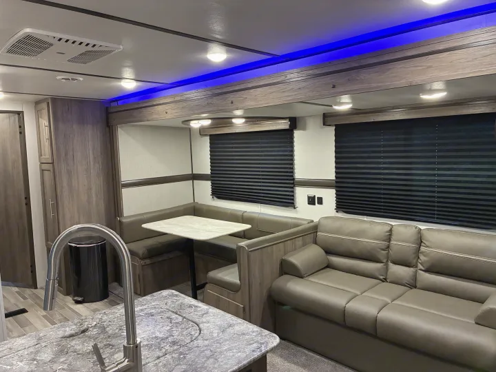 Spacious RV rental interior with dinette, sofa, kitchen counter, and modern blue ceiling accent lights for comfortable travel.. Crossroads RV Zinger 2021