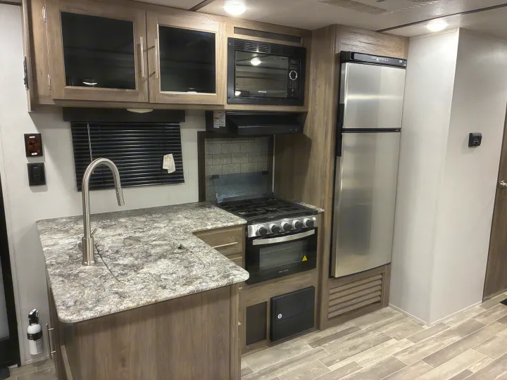 A modern RV rental kitchen featuring stainless steel appliances, a sink, stove, microwave, and wood-grain cabinets.. Crossroads RV Zinger 2021