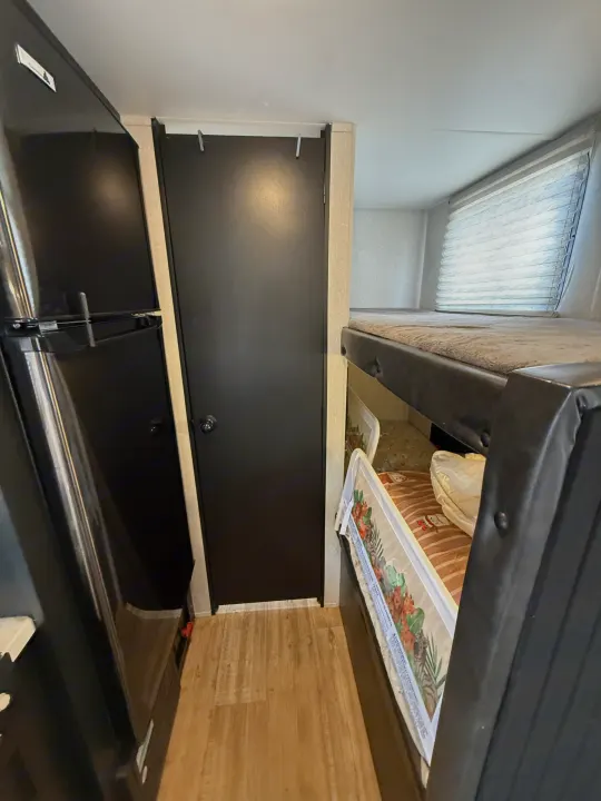 RV rental interior with a black refrigerator, door, and bunk beds, one with a child safety rail, and a window.. Forest River Cherokee Wolf Pup 2021