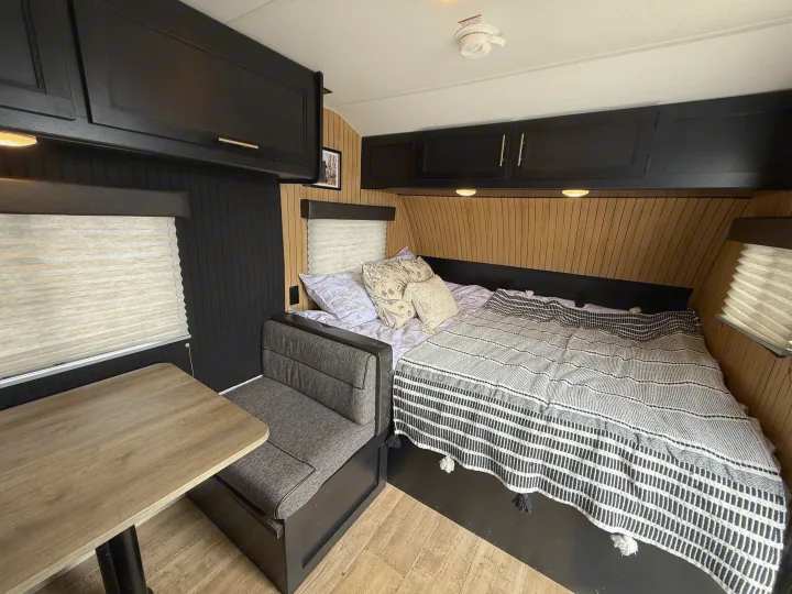 Modern black and wood themed RV rental interior, featuring a comfortable bed with patterned throws and a dinette.. Forest River Cherokee Wolf Pup 2021