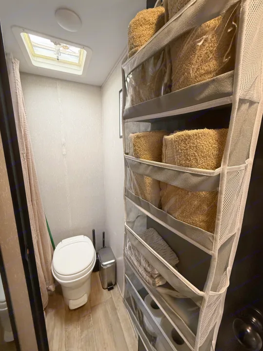 Practical RV rental bathroom with a toilet, shower, overhead vent, and space-saving hanging towel organizer.. Forest River Cherokee Wolf Pup 2021