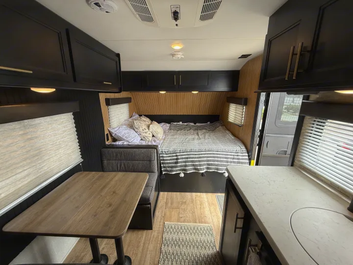Stylish RV rental interior with a cozy bed, dinette, and kitchenette. Features sleek black cabinets and warm wood paneling.. Forest River Cherokee Wolf Pup 2021