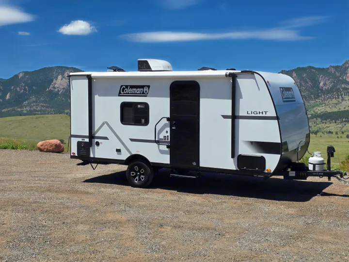 White Coleman Light RV rental parked on gravel with mountains and a clear blue sky in the background.. coleman 17rx 2026