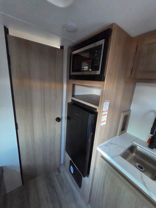 Explore this RV rental's compact kitchen, featuring a built-in microwave, mini-fridge, and sink with marbled counter.. coleman 17rx 2026