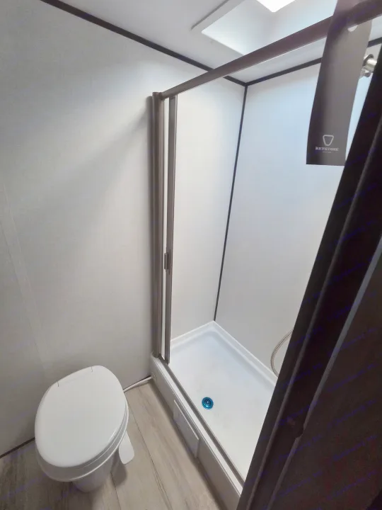 Inside an RV rental: a compact bathroom featuring a white toilet and a corner shower with a blue drain.. coleman 17rx 2026
