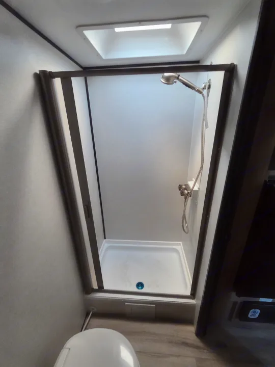 RV rental bathroom features a compact shower stall with a skylight, showerhead, and a white toilet in the foreground.. coleman 17rx 2026