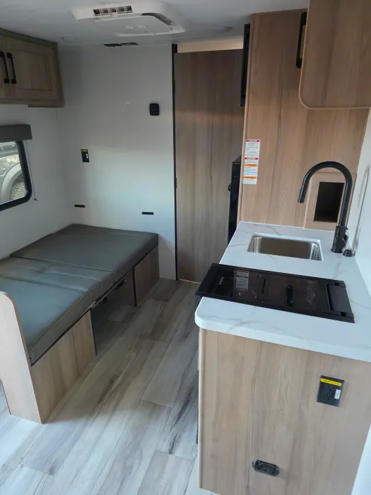 This RV rental interior features a compact kitchen with a sink & stovetop, a comfy dinette/bed, and wood-look flooring.. coleman 17rx 2026