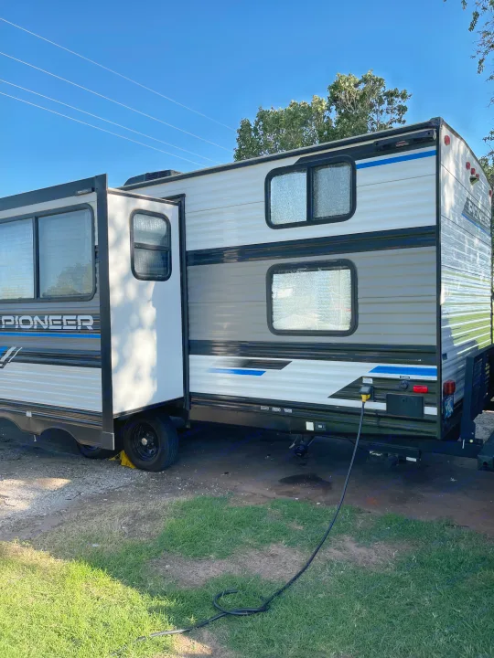 A light-colored 'Pioneer' RV rental, with a slide-out extended and power cord plugged in, parked on grass.. Heartland RVs Pioneer 2023