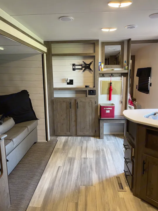 Step into this clean RV rental interior featuring modern wood-look floors, a sofa, built-in media console, and kitchen counter.. Heartland RVs Pioneer 2023