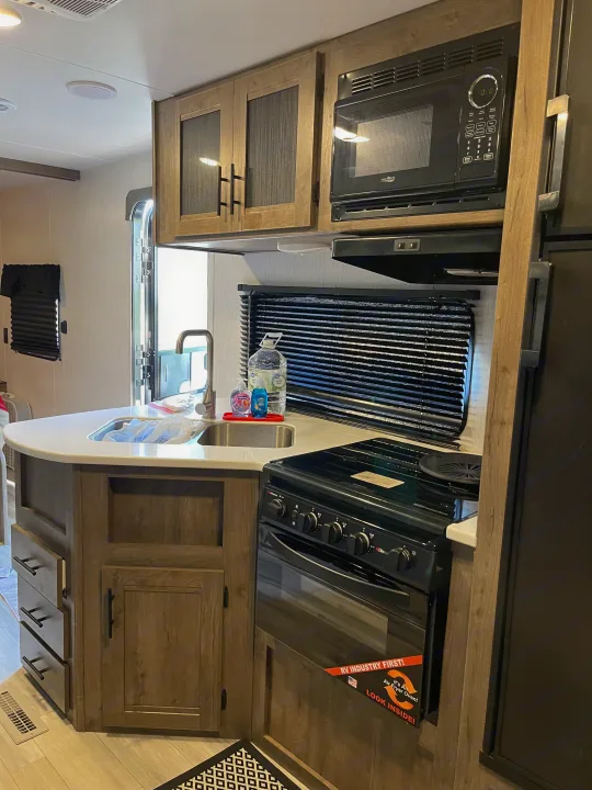 This modern RV rental kitchen features a microwave, sink, stove with a built-in air fryer oven, and wood-toned cabinetry.. Heartland RVs Pioneer 2023