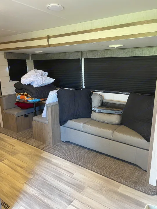 RV rental's cozy interior: a grey dinette and sofa, black window blinds, plus blankets and pillows ready for use.. Heartland RVs Pioneer 2023