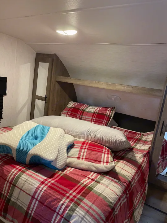 Cozy RV rental bedroom features a bed with red plaid bedding, assorted pillows, and a distinctive blue contoured pillow.. Heartland RVs Pioneer 2023