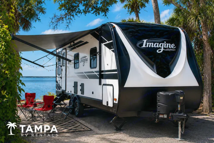 Enjoy this 'Imagine' travel trailer RV rental by the water. Featuring an awning, lights, and red chairs for your perfect camping trip!. Grand Design Imagine 2021