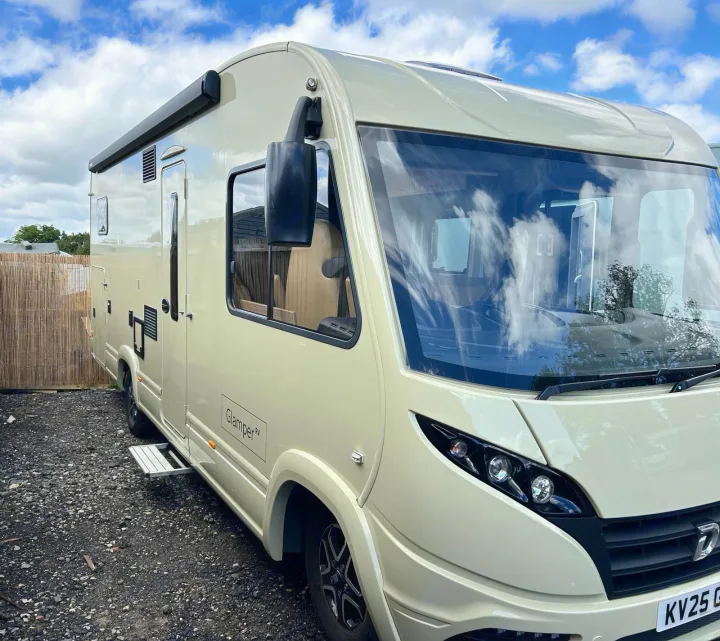 A modern, light beige Glamper RV motorhome for rv rental, parked on gravel under a cloudy blue sky.. GlamperRV DBM Automatic 2025