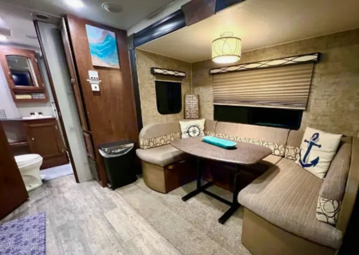 Inviting RV rental interior featuring a U-shaped dinette, windows, and a visible bathroom with a toilet and sink.. Forest River Freedom 2017