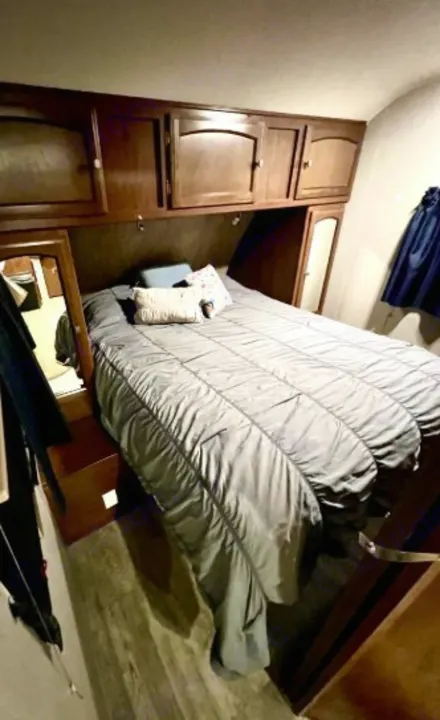 Cozy RV rental bedroom interior featuring a comfy bed, overhead wooden cabinets, and hanging storage for your travel needs.. Forest River Freedom 2017
