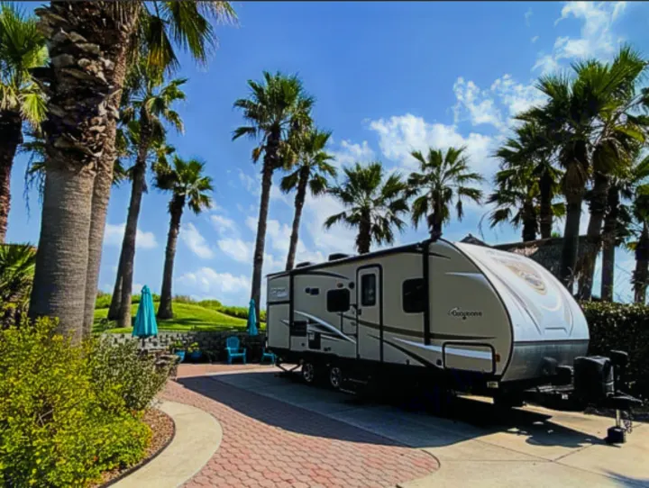 An RV rental is parked at a sunny resort, surrounded by tall palm trees. Ideal for a tropical vacation getaway.. Forest River Freedom 2017