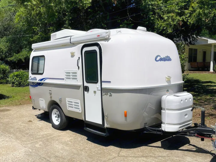 A compact white and grey Casita travel trailer rv rental, a small camper parked on concrete with trees and a house in the background.. Casita Freedom 2024
