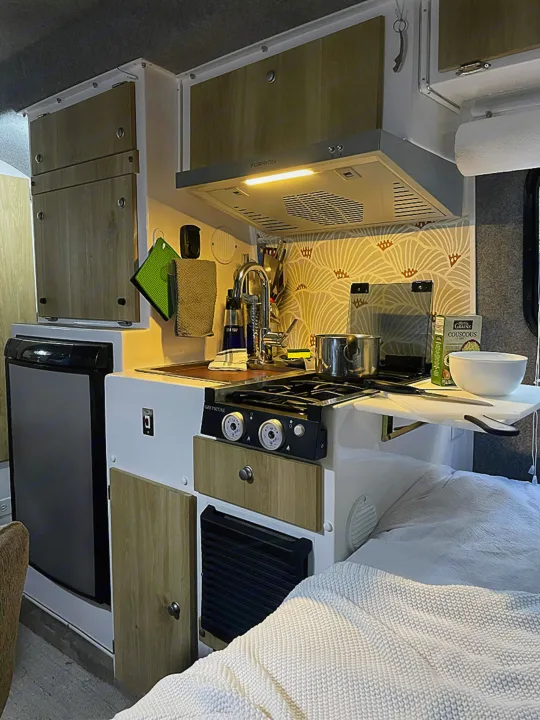This rv rental features a cozy kitchenette with a stove, sink, fridge, and overhead cabinets, alongside a comfortable bed.. Casita Freedom 2024