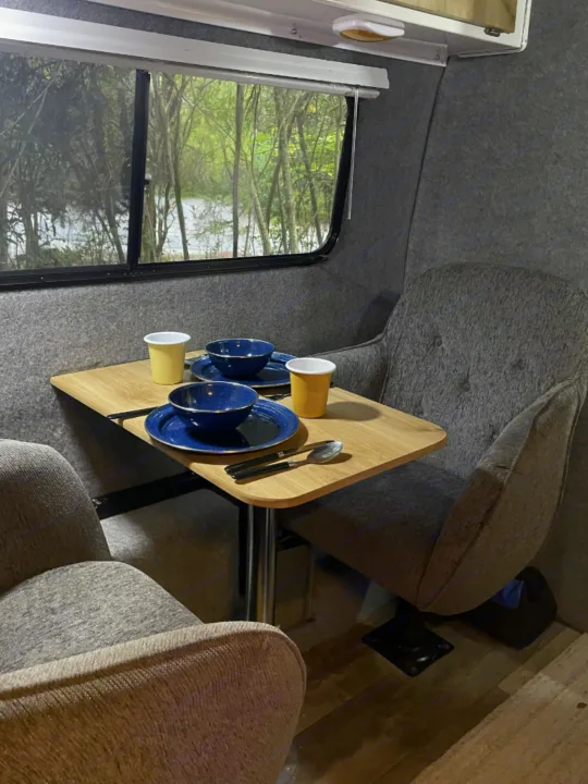 Cozy RV rental dining area for two, with comfy chairs and a scenic window view of trees.. Casita Freedom 2024