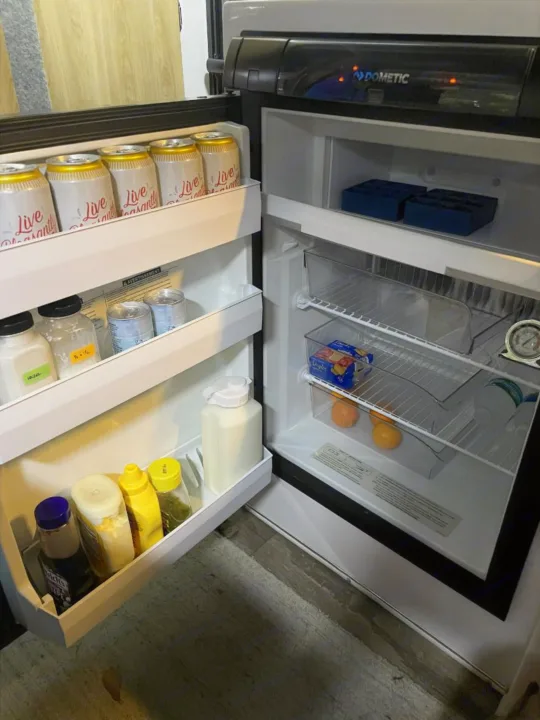 Stocked Dometic refrigerator inside an RV rental, featuring drinks, condiments, canned goods, fruit, and ice trays.. Casita Freedom 2024
