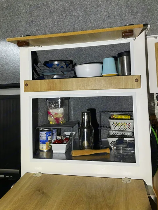 RV rental kitchen cabinet, neatly organized with plates, cups, canned goods, and a cocktail shaker.. Casita Freedom 2024
