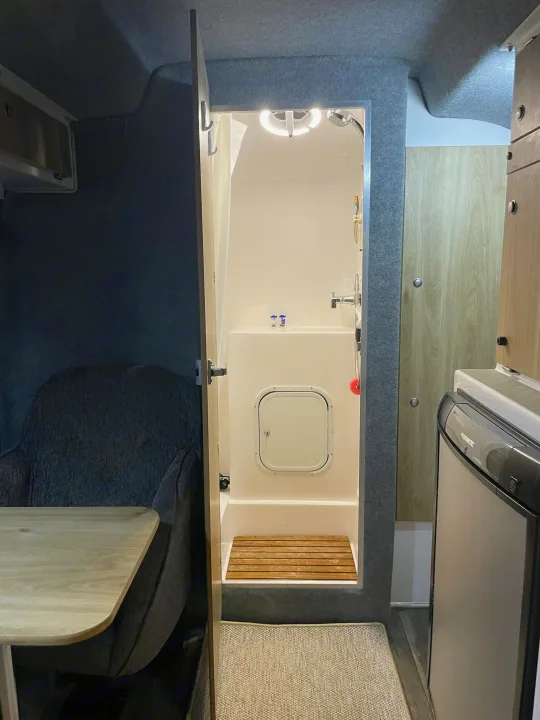 Inside a modern RV rental: a compact shower with wood flooring, cozy seating, and a Dometic fridge.. Casita Freedom 2024