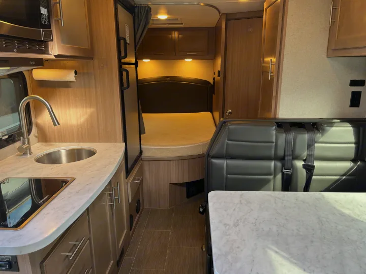 Inside a modern rv rental: kitchen with sink & stovetop, microwave, comfortable bed, and dinette seating with seatbelts.. Adventurer 23 RB 2021
