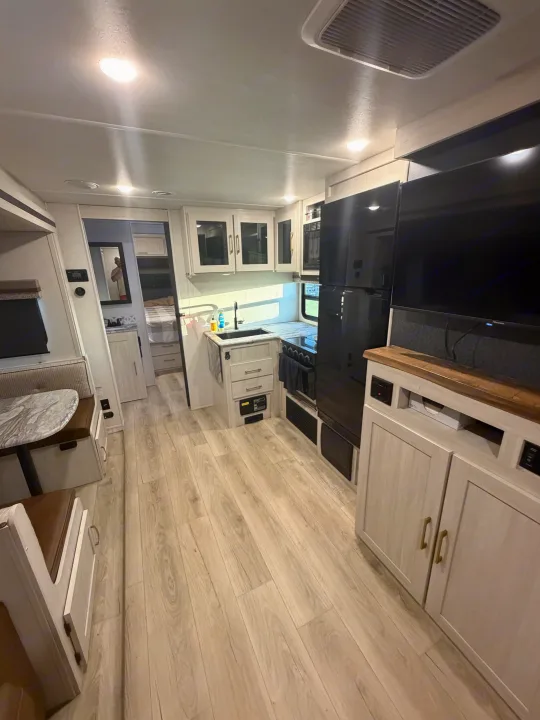 Bright RV rental interior with light wood flooring, a compact kitchen, dinette, and entertainment area.. Forest River Surveyor Legend 2024