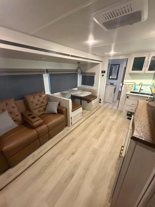 Cozy rv rental interior featuring a brown sofa, dinette, kitchen, and bathroom with light wood-look flooring.. Forest River Surveyor Legend 2024