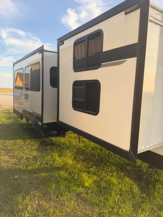 A modern rv rental travel trailer, a Surveyor Legend, with its slide-out extended, parked on green grass under a blue sky.. Forest River Surveyor Legend 2024