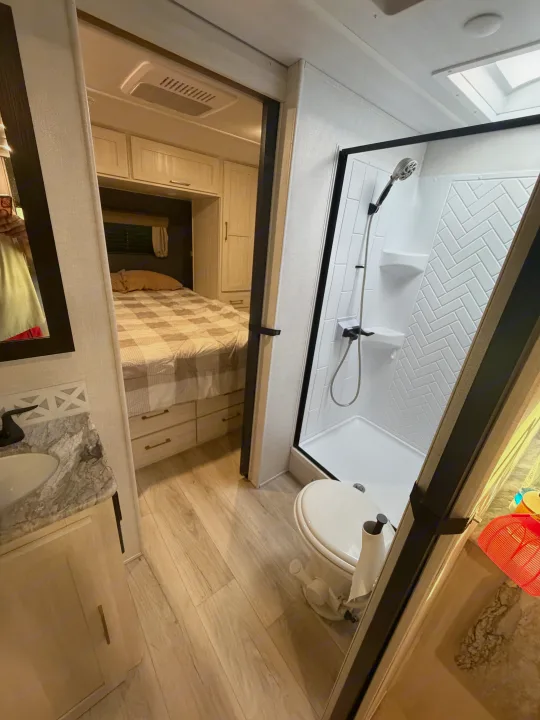Inside this modern rv rental: a compact bathroom with shower, toilet, vanity, and a glimpse into the cozy bedroom.. Forest River Surveyor Legend 2024