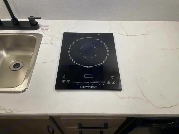 Modern RV rental kitchen features a sleek Greystone induction cooktop and sink on a white, marble-look countertop.. Keystone RV Coleman 13B 2026