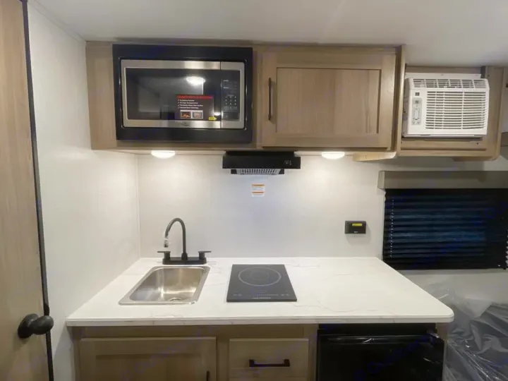 Compact RV rental kitchen features a microwave, sink, induction cooktop, and AC unit, ideal for travel adventures.. Keystone RV Coleman 13B 2026