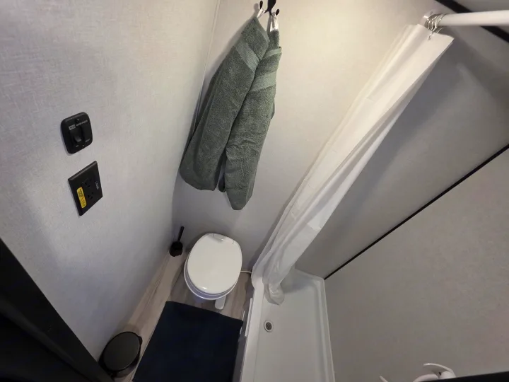 RV rental bathroom features a toilet, shower, water heater switch, and hanging towels, ideal for compact living.. Keystone RV Coleman 13B 2026