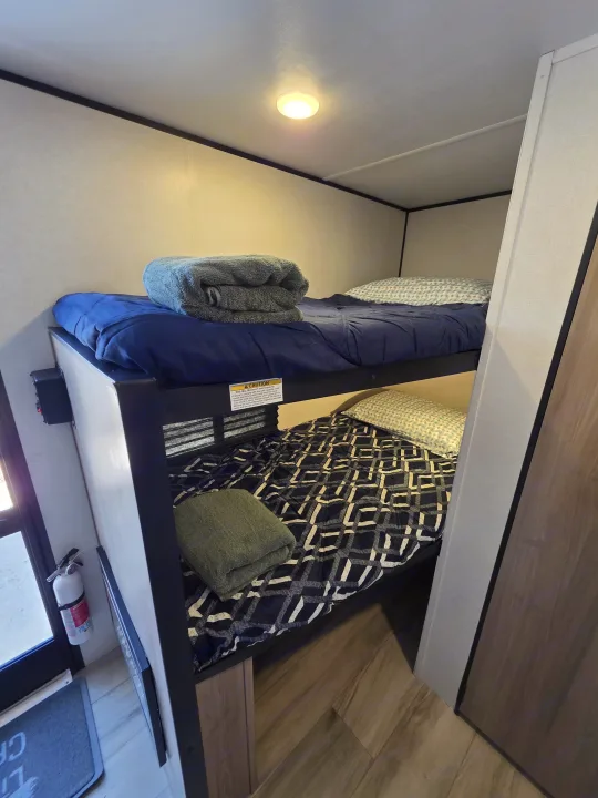 An RV rental's cozy bunk beds, complete with fresh bedding, pillows, and folded towels on both top and bottom bunks.. Keystone RV Coleman 13B 2026