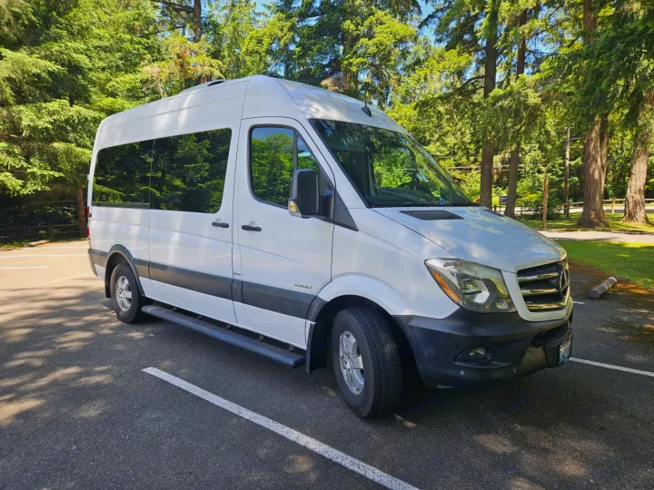 A white Mercedes Sprinter van, ideal for rv rental, is parked in a sunny wooded area. Perfect for outdoor adventures.. Mercedes-Benz Sprinter 2016