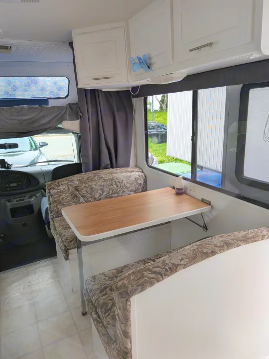 Inside this rv rental: A cozy dinette with patterned cushions, wooden table, white cabinets, and view into the driver's cabin and outside through windows.. Ford Ford 2001