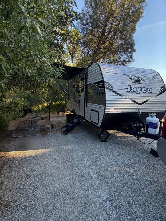 Enjoying an RV rental! A silver Jayco travel trailer parked at a gravel campsite with a picnic table and lush trees.. Jayco Jay Flight SLX 2026