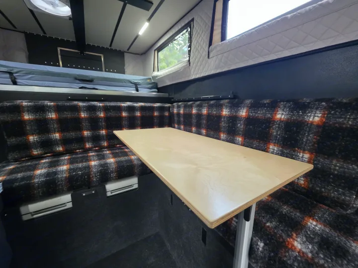 Cozy RV rental interior with a plaid U-dinette, wooden table, and elevated bed platform for comfortable travel.. Ford F350 2025