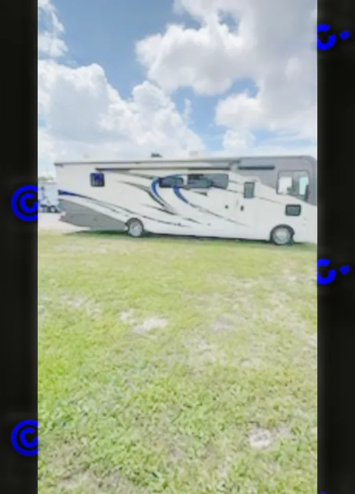 Modern white and blue Class A motorhome rv rental, ready for travel. Parked on grass beneath a partly cloudy sky.. Fleetwood FLAIR 2020