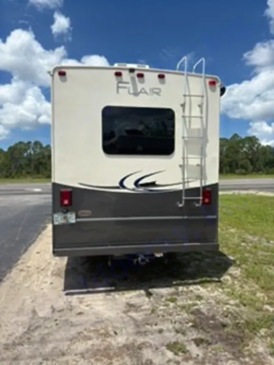 Rear of a white and gray RV rental, featuring a ladder and tinted window, parked outdoors. Ready for your next travel adventure.. Fleetwood FLAIR 2020