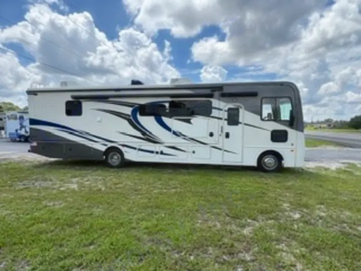 This spacious white and gray motorhome, perfect for your next RV rental trip, is parked on grass under a cloudy sky.. Fleetwood FLAIR 2020