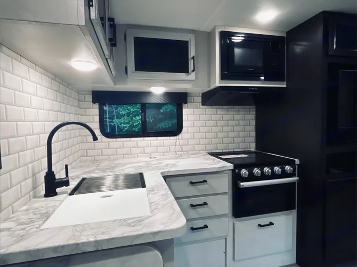 Sleek modern RV rental kitchen featuring white subway tile, marble-look counters, black faucet, microwave, oven, and cabinets.. Jayco Jay Feather 2022