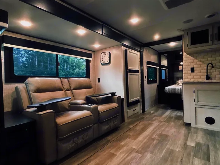 Modern rv rental interior with plush recliners, large windows, a kitchenette, and a cozy bedroom area.. Jayco Jay Feather 2022