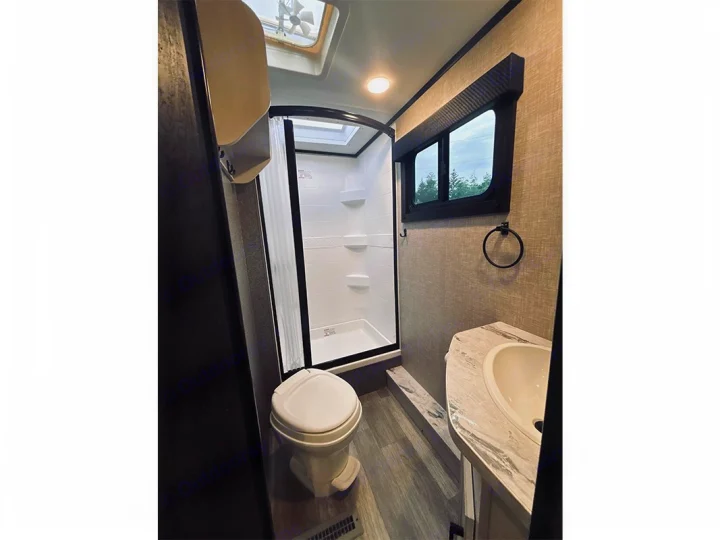 This RV rental bathroom features a toilet, standing shower, sink, and natural light from a window and ceiling fan.. Jayco Jay Feather 2022